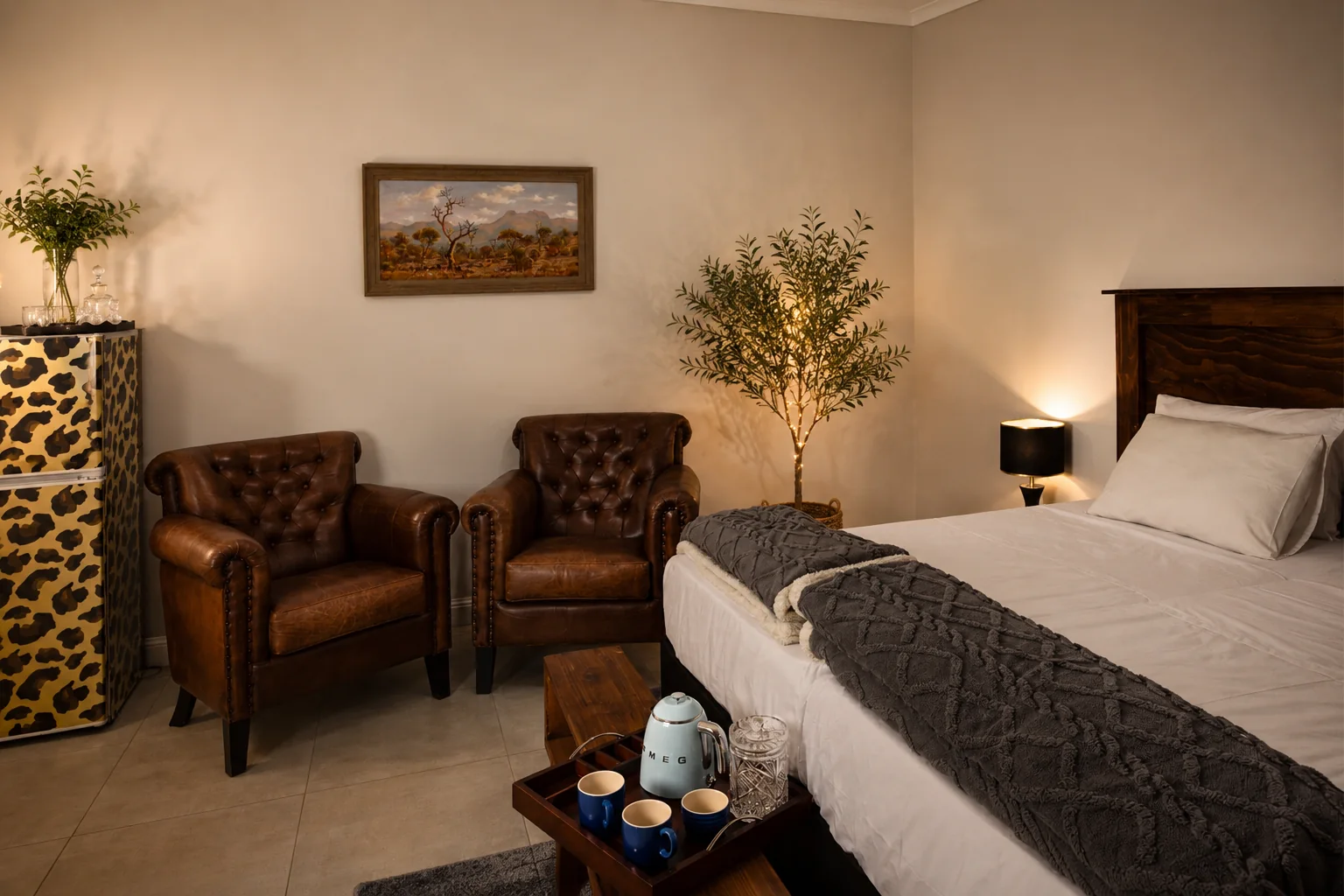 Komati Art Retreat bedroom with a made bed, two leather armchairs and a tea tray